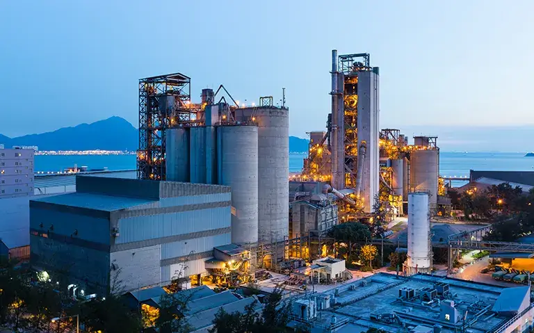 A cement factory at dusk with the ocean in the background specializing in Project Engineering Services